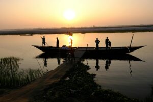 Silhouetted people on a boat at sunrise on a tranquil river.