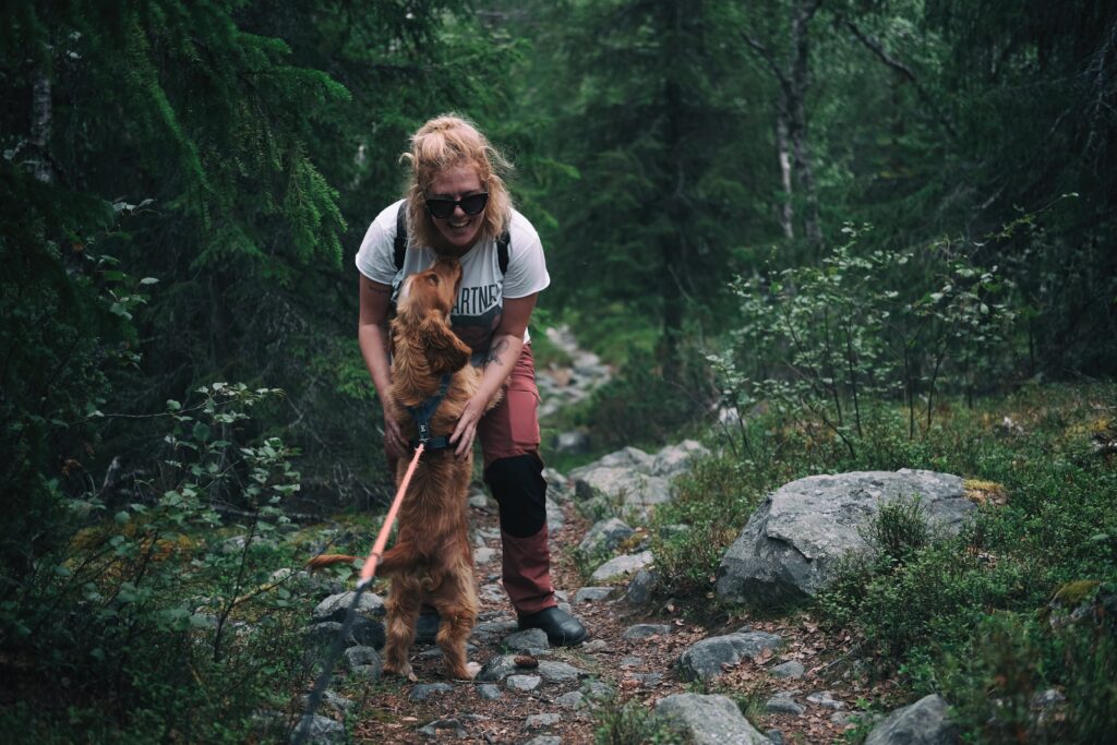 A woman playfully interacting with her dog on a forest trail in Sweden by day.