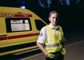 Female paramedic in reflective vest beside ambulance on city street at night.