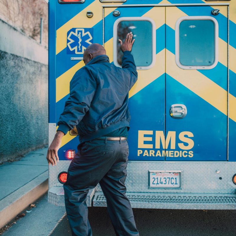 A paramedic in action behind an EMS ambulance on a city street during the day.